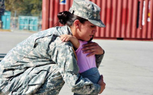 an image of a female soldier in Army fatigues crouching down to hug a small toddler baby